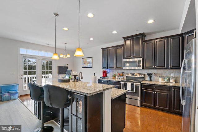 kitchen with a kitchen breakfast bar, pendant lighting, backsplash, an island with sink, and stainless steel appliances