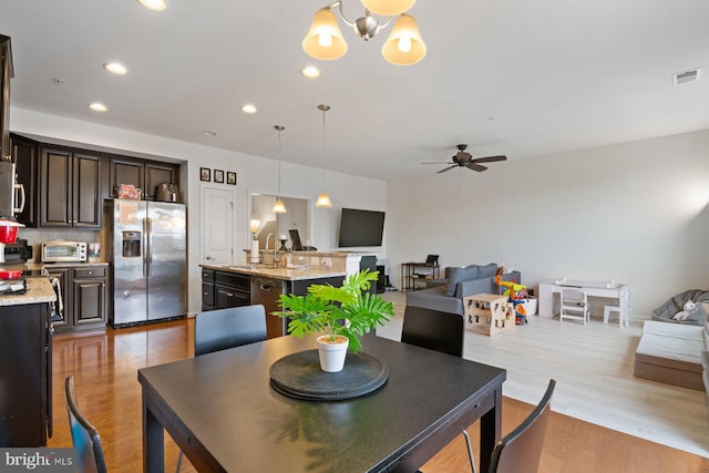 dining room featuring ceiling fan with notable chandelier, sink, and light wood-type flooring