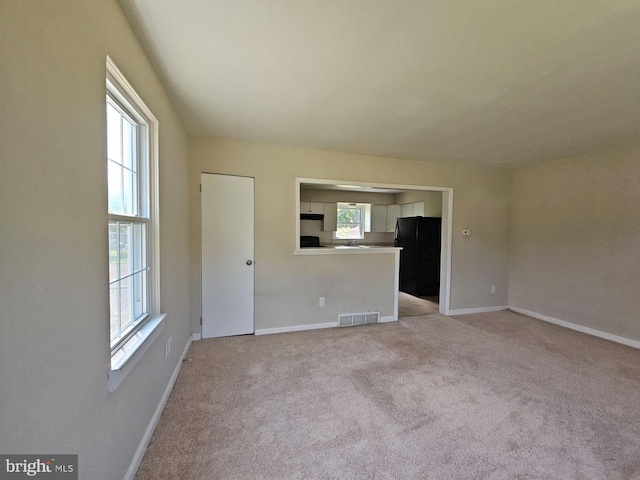 unfurnished living room with light colored carpet and a wealth of natural light