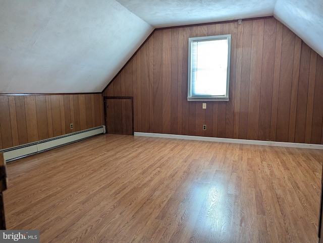 bonus room featuring light hardwood / wood-style floors, baseboard heating, wooden walls, and vaulted ceiling