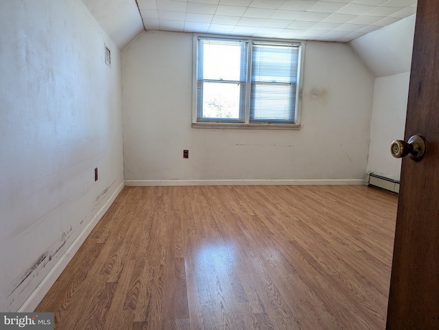 additional living space with a baseboard heating unit, vaulted ceiling, and light hardwood / wood-style flooring