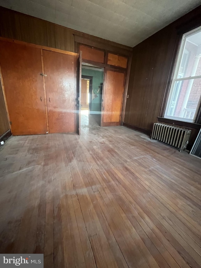 unfurnished bedroom with radiator, wood walls, and light wood-type flooring