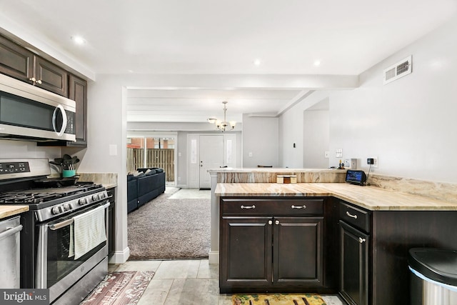 kitchen with appliances with stainless steel finishes, a chandelier, light colored carpet, and dark brown cabinetry