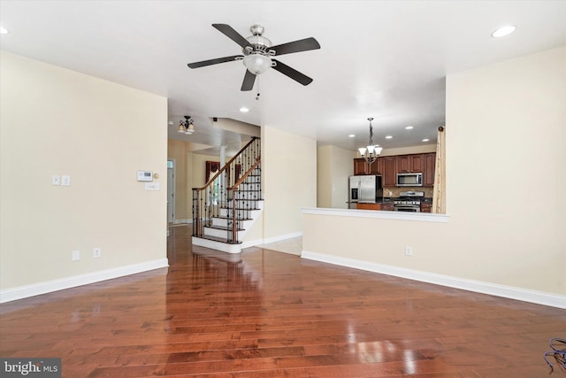 unfurnished living room with ceiling fan with notable chandelier and dark wood-type flooring