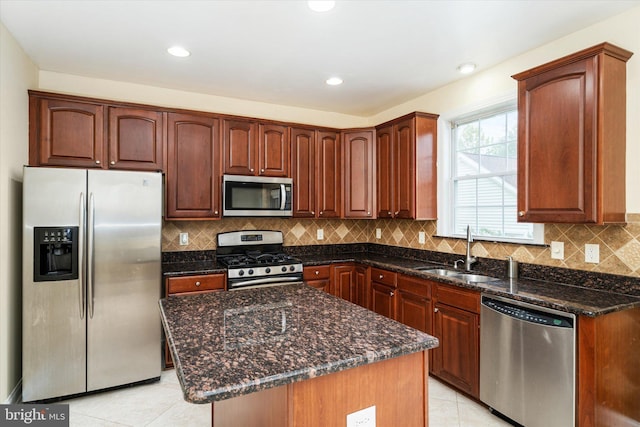 kitchen with light tile patterned floors, stainless steel appliances, dark stone counters, a kitchen island, and sink