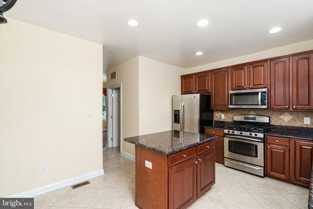 kitchen featuring light tile patterned floors, appliances with stainless steel finishes, decorative backsplash, dark stone countertops, and a kitchen island