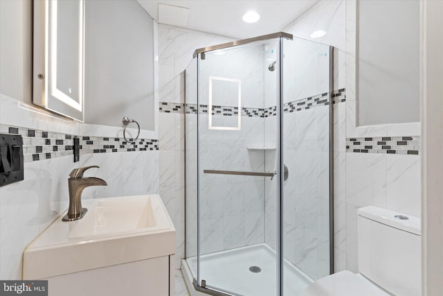 bathroom featuring toilet, tile walls, a shower with door, and vanity