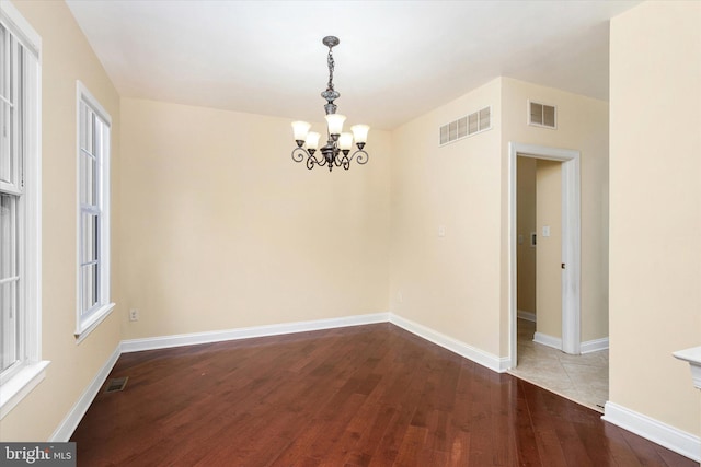 empty room featuring wood-type flooring and an inviting chandelier