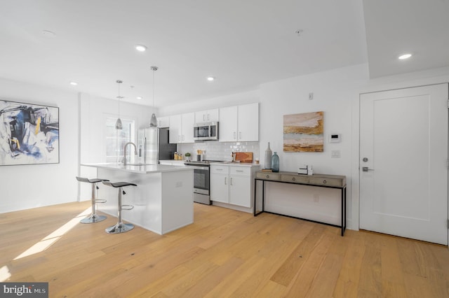 kitchen featuring hanging light fixtures, stainless steel appliances, tasteful backsplash, white cabinets, and sink