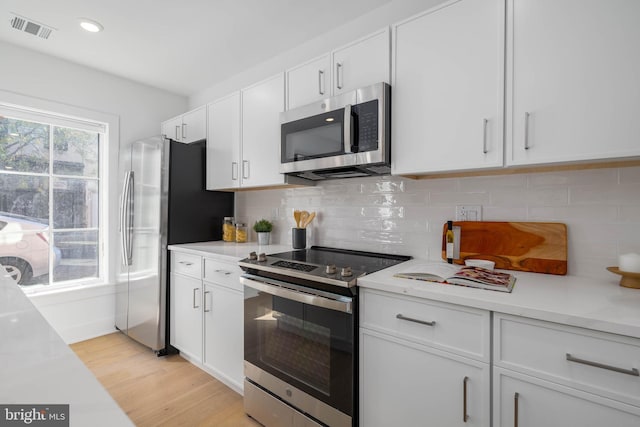 kitchen featuring backsplash, white cabinets, appliances with stainless steel finishes, and light hardwood / wood-style flooring