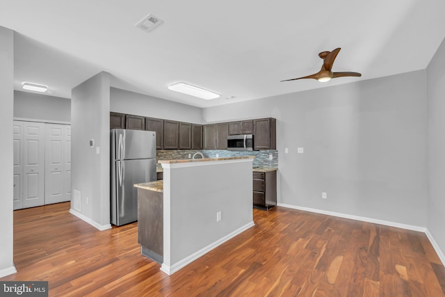 kitchen with dark brown cabinets, backsplash, dark hardwood / wood-style floors, a center island with sink, and stainless steel appliances