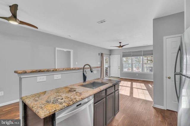 kitchen with dark brown cabinetry, stainless steel appliances, sink, ceiling fan, and a center island with sink