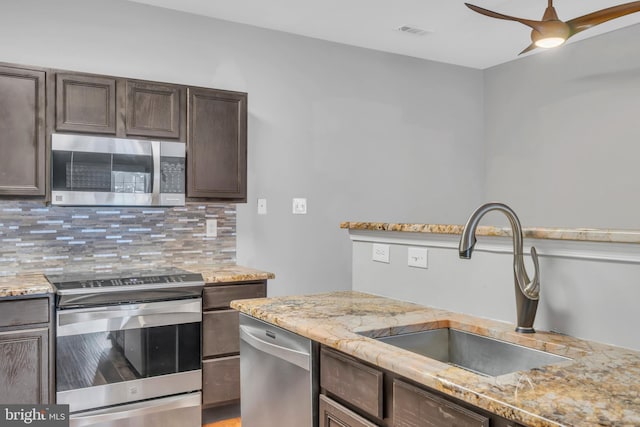 kitchen with sink, stainless steel appliances, light stone countertops, decorative backsplash, and dark brown cabinetry