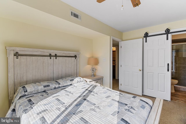 bedroom with ceiling fan, ensuite bathroom, a barn door, and carpet flooring