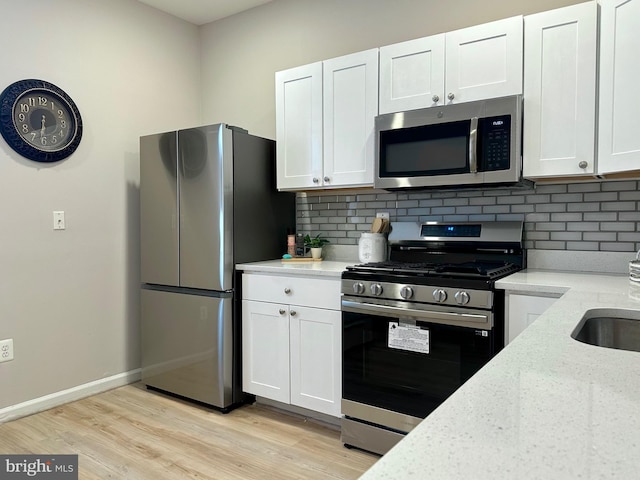 kitchen with stainless steel appliances, white cabinets, light hardwood / wood-style flooring, decorative backsplash, and light stone countertops