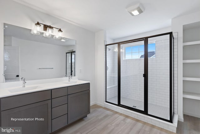 bathroom with double vanity, a stall shower, wood finished floors, and a sink