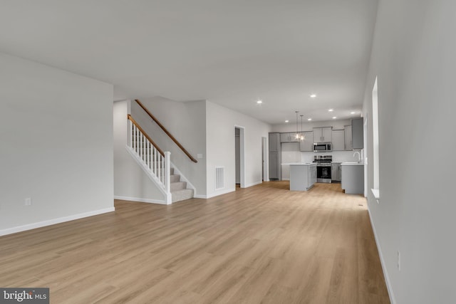 unfurnished living room featuring light wood finished floors, baseboards, stairway, recessed lighting, and a sink