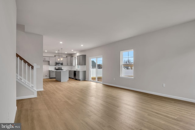 unfurnished living room with stairs, recessed lighting, light wood-style floors, and baseboards