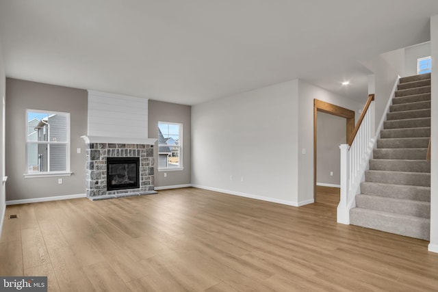 unfurnished living room with stairs, a stone fireplace, light wood-style flooring, and baseboards