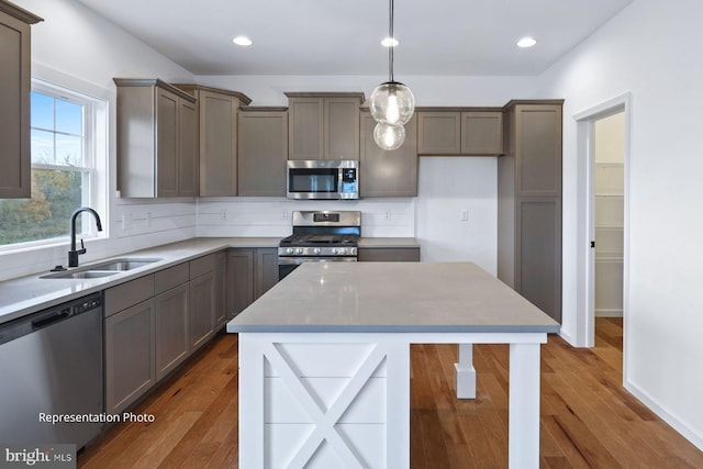 kitchen with pendant lighting, stainless steel appliances, a kitchen island, wood-type flooring, and sink