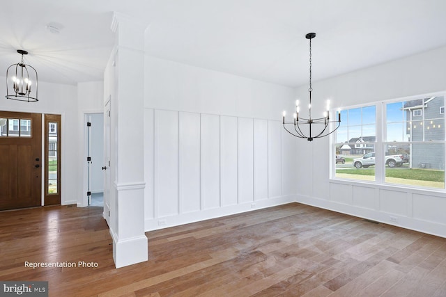 unfurnished dining area with wood finished floors, a chandelier, and a decorative wall