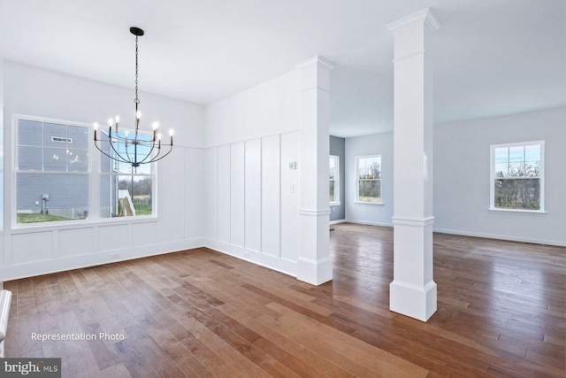 unfurnished dining area with decorative columns, baseboards, a notable chandelier, and wood finished floors