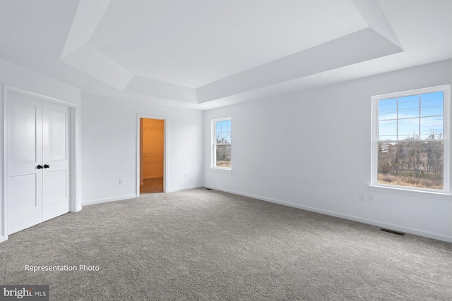 unfurnished bedroom featuring a closet, baseboards, a tray ceiling, and carpet floors