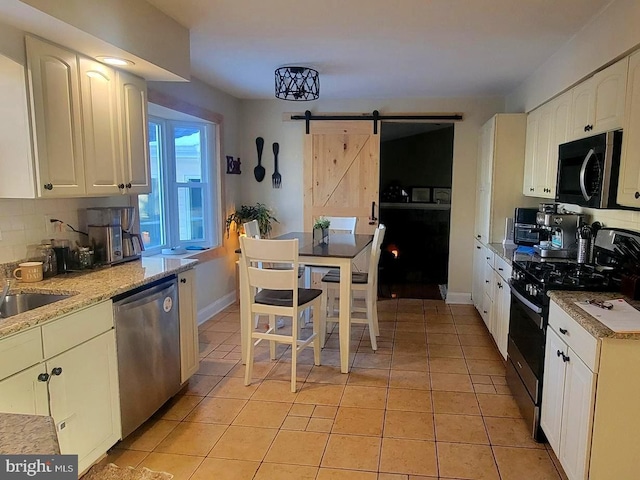 kitchen with stainless steel appliances, a barn door, light tile patterned floors, and white cabinetry