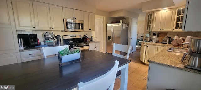 kitchen with appliances with stainless steel finishes, light stone countertops, light tile patterned flooring, white cabinetry, and backsplash