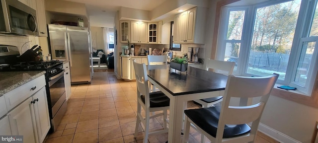 kitchen with stainless steel appliances, dark stone counters, light tile patterned floors, and decorative backsplash