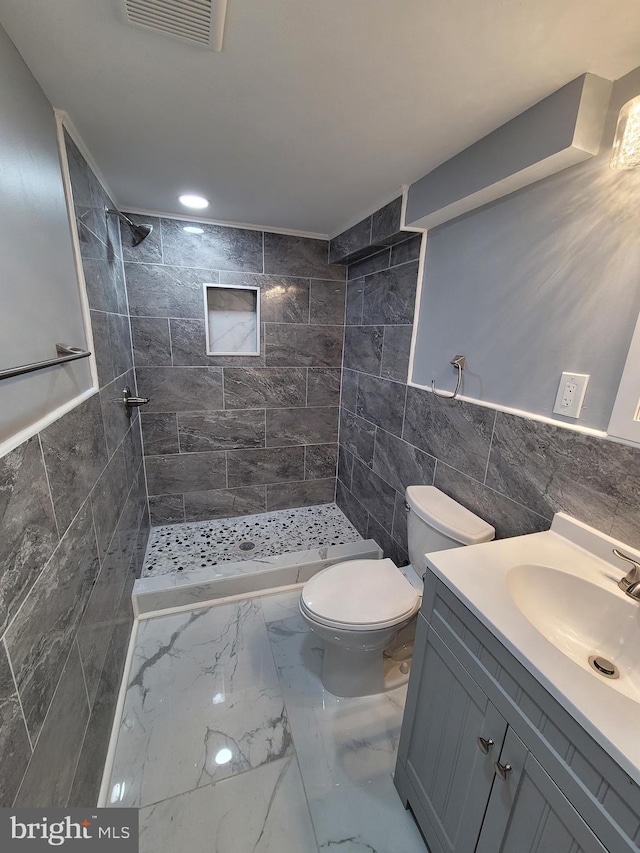 bathroom with tile walls, toilet, tiled shower, and vanity