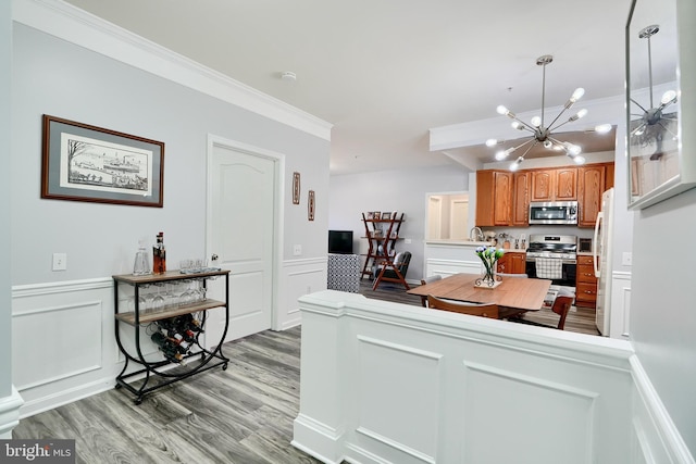 kitchen featuring a chandelier, decorative light fixtures, hardwood / wood-style floors, crown molding, and appliances with stainless steel finishes