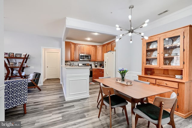 dining area with an inviting chandelier, light wood-type flooring, and ornamental molding