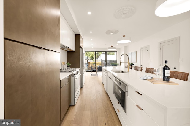 kitchen with a kitchen island with sink, appliances with stainless steel finishes, white cabinets, decorative light fixtures, and sink