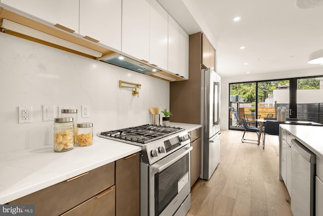 kitchen featuring stainless steel appliances, white cabinetry, light hardwood / wood-style floors, a wall of windows, and backsplash