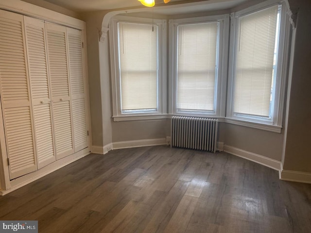 unfurnished bedroom with a closet, radiator heating unit, multiple windows, and dark hardwood / wood-style floors