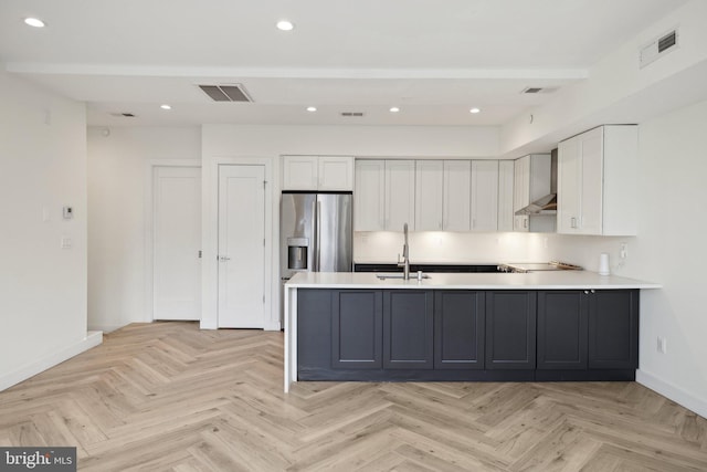 kitchen with white cabinetry, sink, light parquet floors, stainless steel refrigerator with ice dispenser, and wall chimney exhaust hood