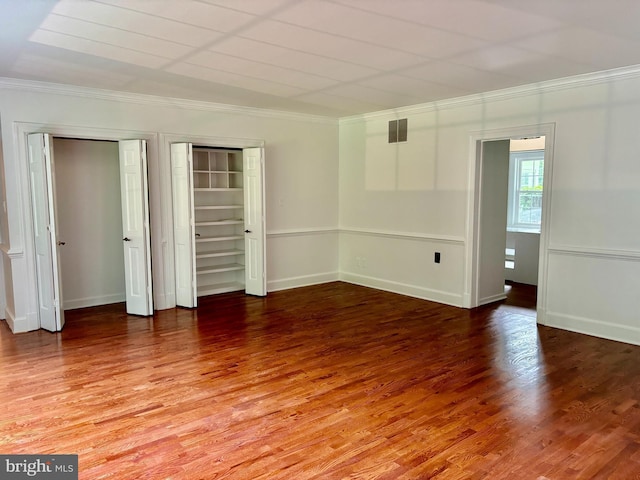 unfurnished bedroom with ornamental molding, multiple closets, and hardwood / wood-style floors