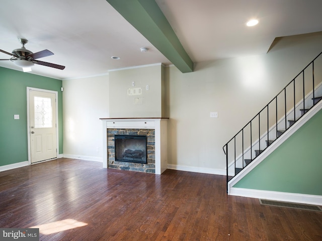 unfurnished living room featuring dark hardwood / wood-style flooring, ceiling fan, a stone fireplace, and beamed ceiling