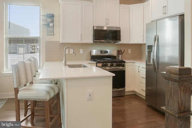 kitchen featuring appliances with stainless steel finishes, white cabinetry, sink, kitchen peninsula, and a breakfast bar