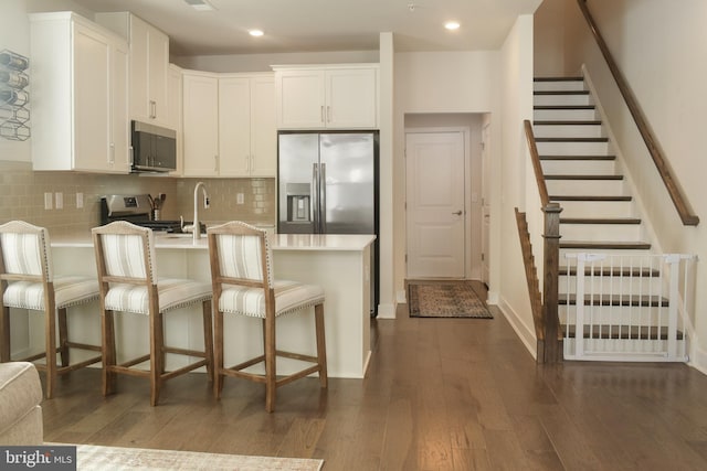 kitchen featuring a kitchen bar, appliances with stainless steel finishes, white cabinets, dark hardwood / wood-style flooring, and backsplash