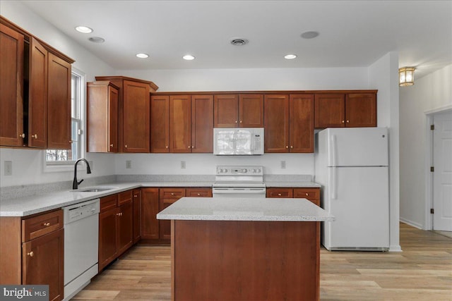 kitchen with light stone countertops, white appliances, a kitchen island, sink, and light hardwood / wood-style flooring