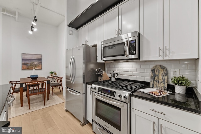 kitchen with stainless steel appliances, dark stone countertops, white cabinets, and light hardwood / wood-style floors