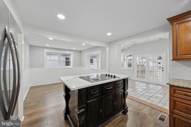 kitchen with stainless steel fridge, light hardwood / wood-style floors, a kitchen island, black electric stovetop, and backsplash