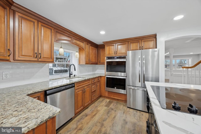 kitchen with appliances with stainless steel finishes, light stone countertops, sink, light hardwood / wood-style flooring, and backsplash