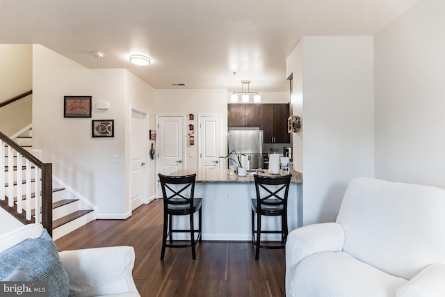 kitchen with a breakfast bar, dark brown cabinets, dark hardwood / wood-style flooring, stainless steel fridge, and light stone countertops