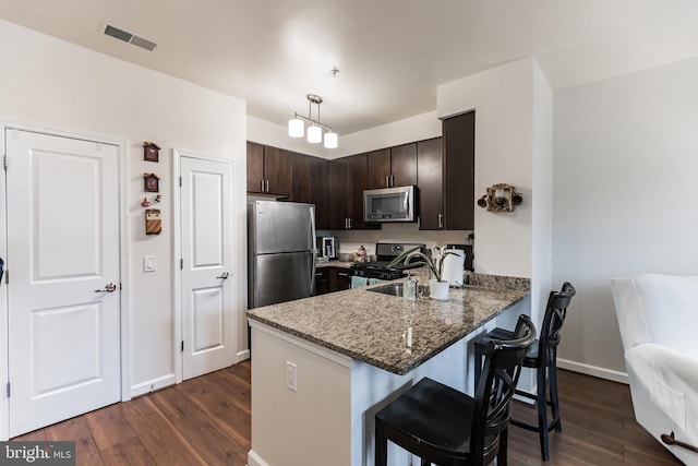 kitchen with dark hardwood / wood-style floors, decorative light fixtures, a kitchen breakfast bar, dark brown cabinetry, and stainless steel appliances