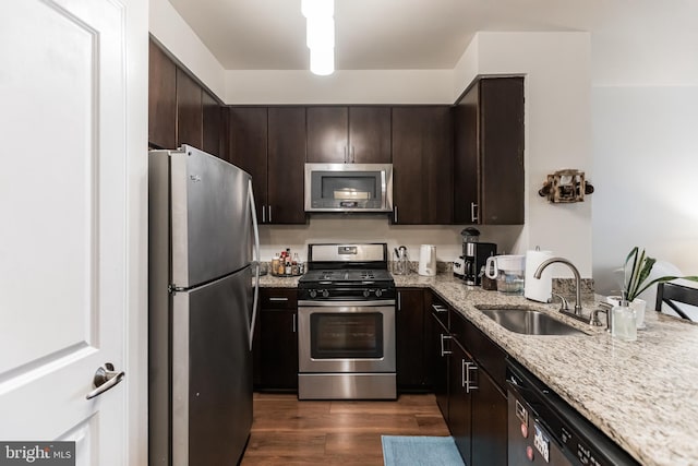 kitchen with sink, dark hardwood / wood-style flooring, light stone counters, dark brown cabinetry, and stainless steel appliances