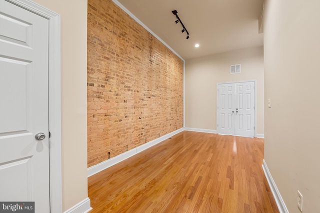 hallway featuring brick wall, track lighting, and light hardwood / wood-style flooring