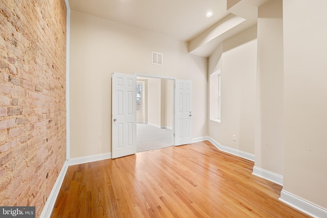 empty room with hardwood / wood-style flooring and brick wall